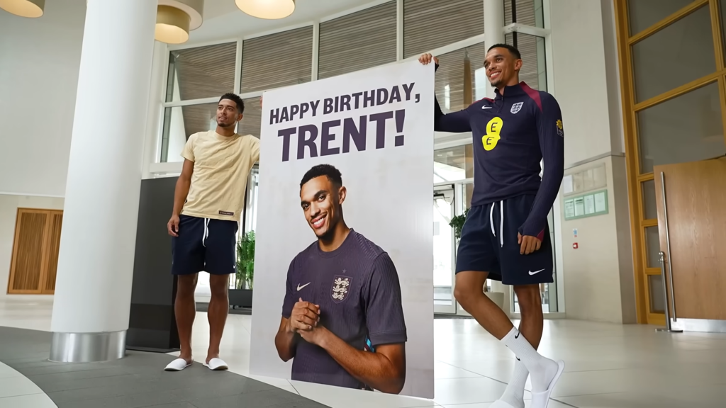 Jude Bellingham and Trent Alexander-Arnold stand next to a giant birthday card with the text 'Happy Birthday, Trent!'